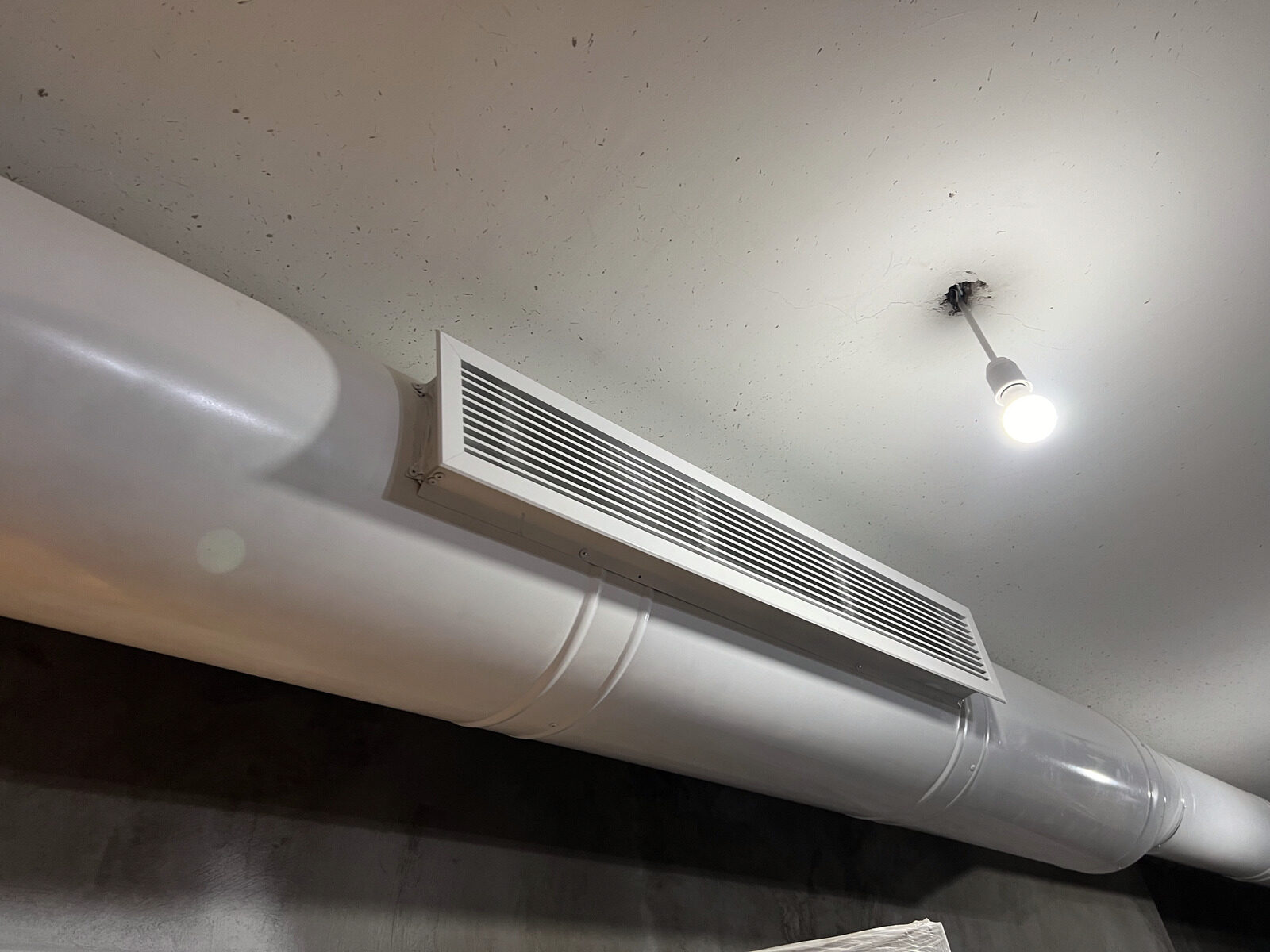 A ducted air conditioning grille finished in a ceiling next to a pendant light.