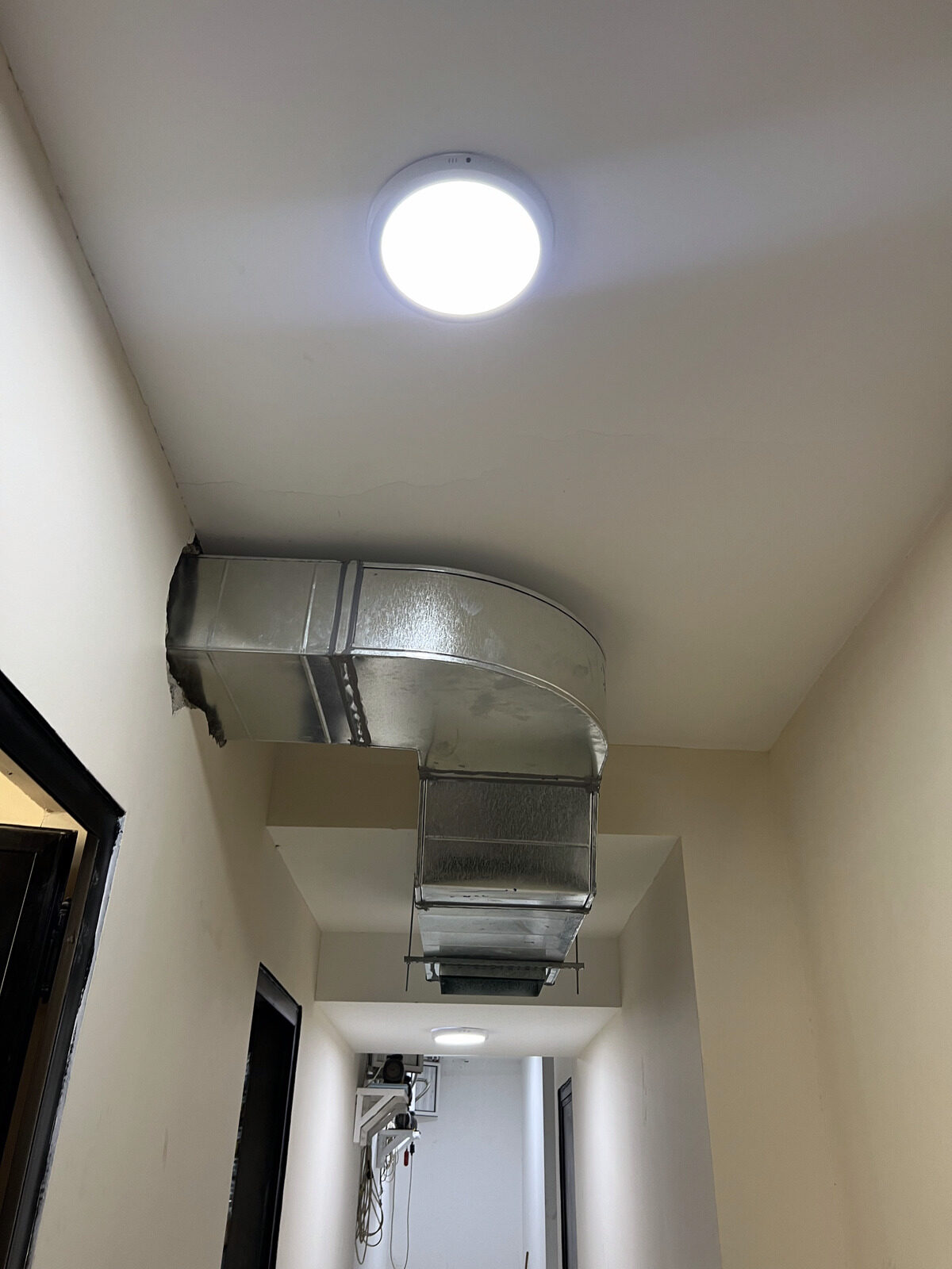 A round ceiling diffuser and ductwork elbow finished in a hallway.