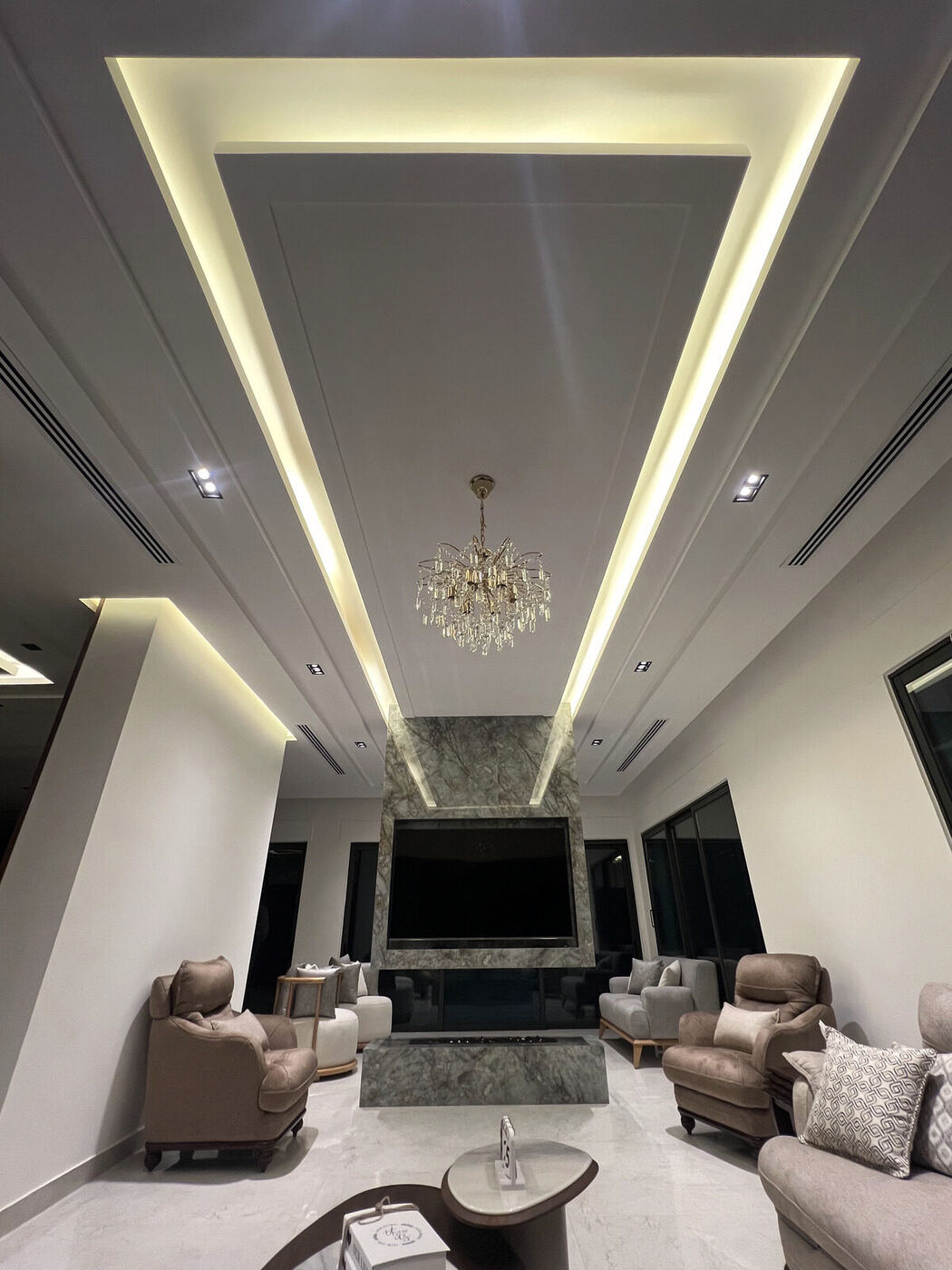 Central AC diffusers integrated into a villa living room's ceiling design, with a chandelier.