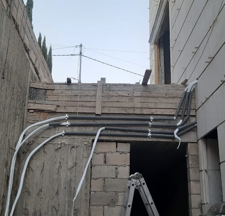 Conduit and refrigerant lines routed along an unfinished exterior wall during construction.
