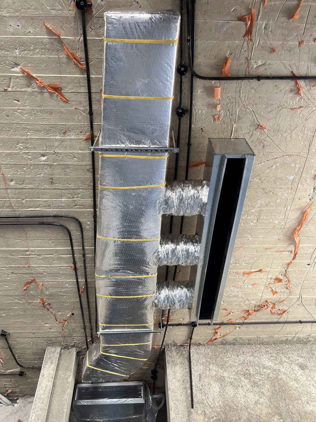 Insulated ductwork trunk connected to a fan-coil unit through a concrete slab opening.