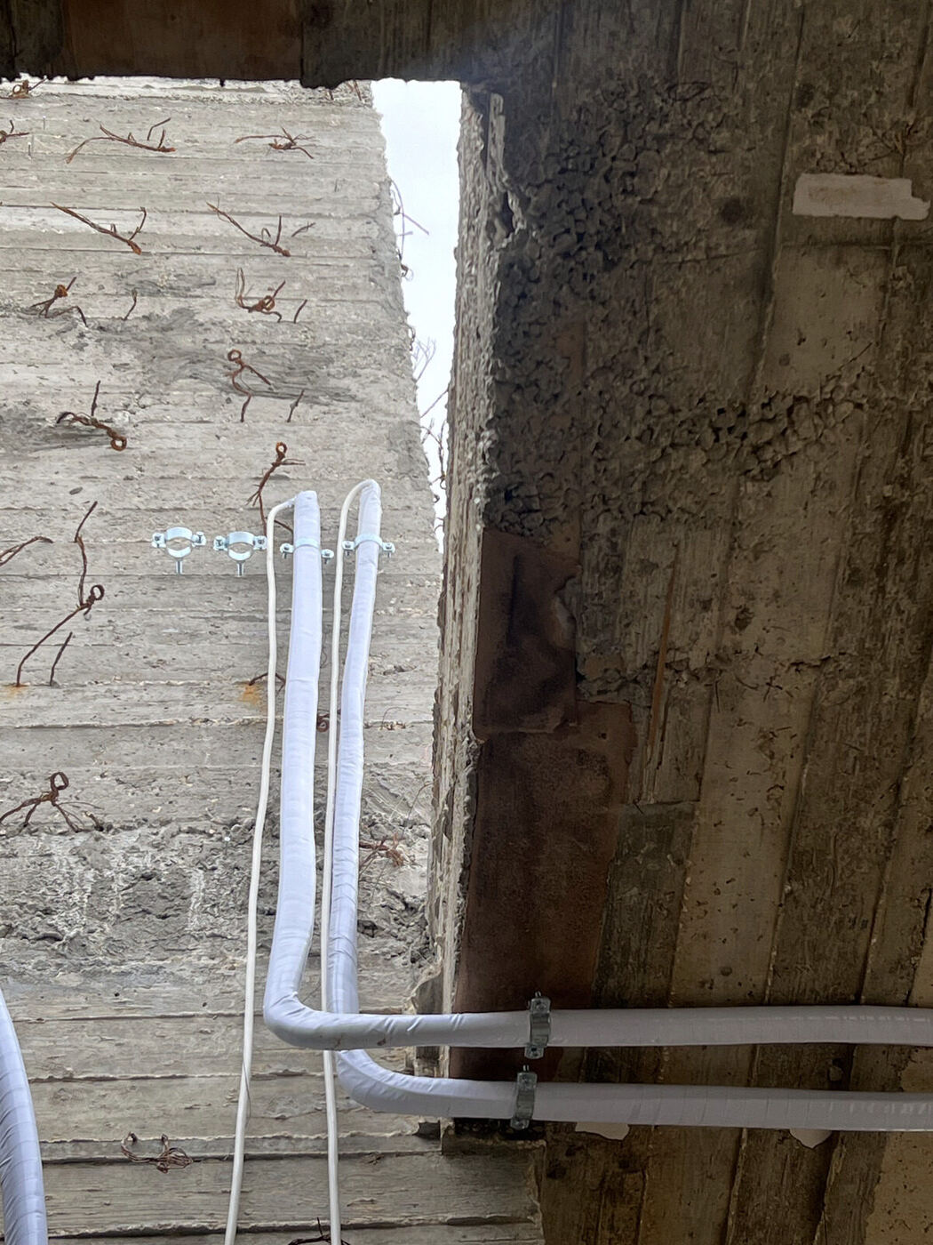 Refrigerant lines run down through a concrete slab opening on a construction site.