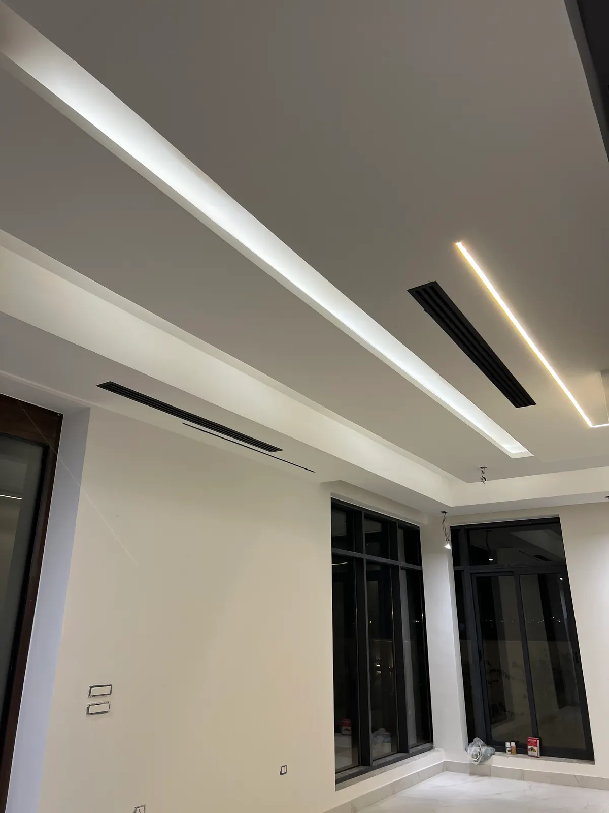 Black central-AC linear diffusers with cove lighting in the ceiling of a finished villa lounge.