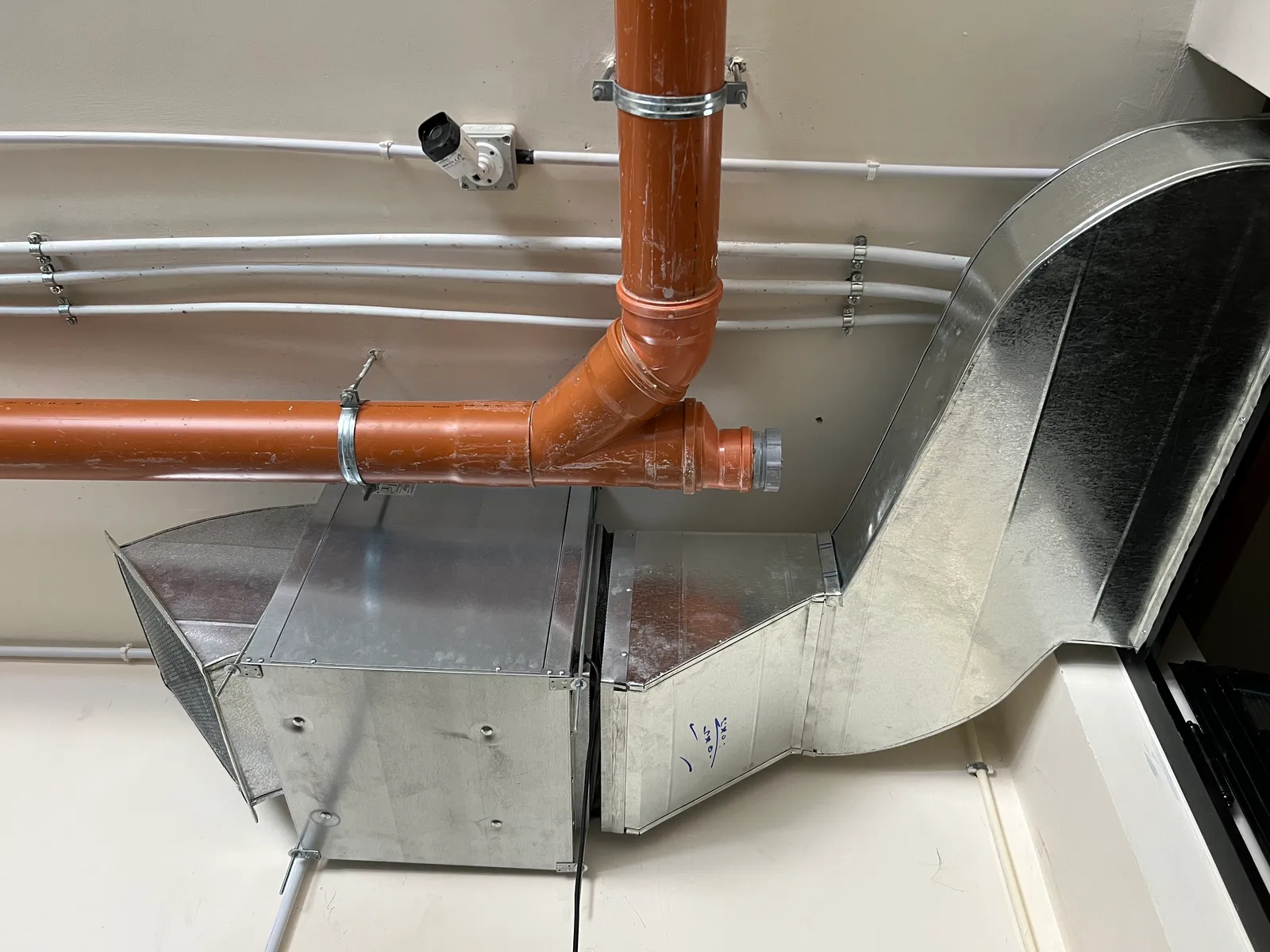 Galvanized sheet-metal air ducts with a plenum box, a curved transition and a PVC drain line in a service room.